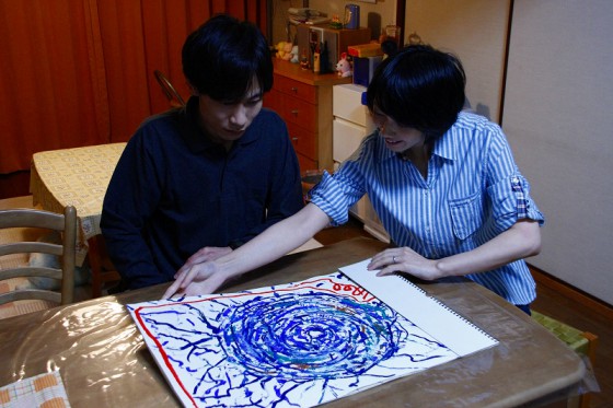 自閉症の長男が描いた「蜘蛛の巣」を見る夫婦。 この絵は映画のテーマの一つにもなっている。